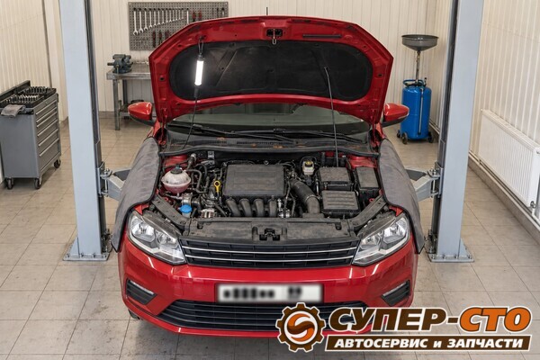 Volkswagen Polo на подъёмнике, капот открыт, на крыльях защитные накидки, под капотом лампа
